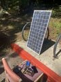 A picture of a prototype including the solar panel and electrical parts sitting on a chair - along with a phone being charged by the setup!