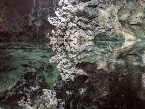 Reflection of a white rocky cave wall that meets the surface of a very clear and light blue lake. The reflection has no ripples and creates a somewhat geometric shape