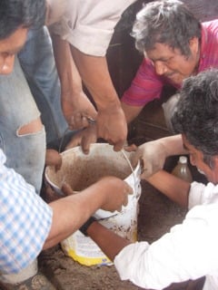 Villagers working together to remove the bucket mold from the primary combustion chamber of their new Lorena Cookstove