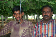 Farmer Jayashankar and his son. The hanging pipe is used to water their crop of grapes. This drip irrigation method has enabled Jayashankar