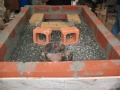 The Novaceramic Vintex brick was cut in equal halves and positioned in the gravel to serve as support structures for the channels that connect the primary combustion chamber to the secondary burners. For accurate positioning, the primary (larger) burner was momentarily placed on top of the combustion chamber and the secondary burner mold placed close to the chimney inlets (see EPMC for details)