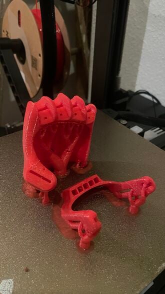 The image shows the main body and wrist-mounted actuator on a 3D-printers bed printed from red PETG.