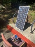 A picture of a prototype including the solar panel and electrical parts sitting on a chair - along with a phone being charged by the setup!