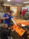 Use a mallet and a piece of wood to hammer the road sign that is set against a sharp, straight edge.