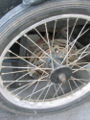 The trike rear wheels are modified front wheels from a motocross-dirt bike motorcycle. The disk brake calipers and rotor are also from the same type of motorcycle. The hub's 5/8" tapered bore was bored out to a 2" straight cylindrical bore on a lathe so that a cylindrical stainless steel sleeve fits between the axle and the wheel hub. This buttresses the wheel hub and allows the wheel to be cantilevered instead of being supported by a fork assembly as originally intended by the engineers who designed it. The rear wheels of the trike are also driven rather then free-wheeling as originally intended for the front wheel of a motorcycle. This was accomplished by bolting the sleve's flang to the same bolts that attach the disk rotor to the hub. The sleeve and axle are keyed together so that they spin in unison. The calipers are mounted on a strong bracket, custom fabricated for that purpose. The trike also has a set of drum brakes.