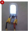 Un-hook wires from volt meter, and hook the wires to the light. Set up with the light oriented as shown in the picture. Clip the red wire on the positive terminal (right side) of the light and the black wire to the negative terminal (left side). Crank the drill to power the electronics.