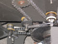 A close up view of system used to tension the motor chain drive. Each of the two chains are connected by an intermediate drive shaft. Each chain is suspended by two skateboard wheels, connected by springs. The tensioned side of the chain is reversed when switching from forward drive to reverse or from forward drive to regenerative breaking. This system provides for a smooth transition.